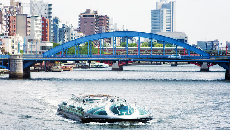 View of a boat on the water with a blue bridge and cityscape in the background. 