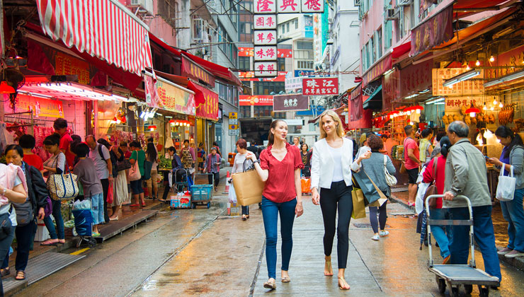 A couple of friends walk down a busy, colorful street in Hong with shopping bags.
