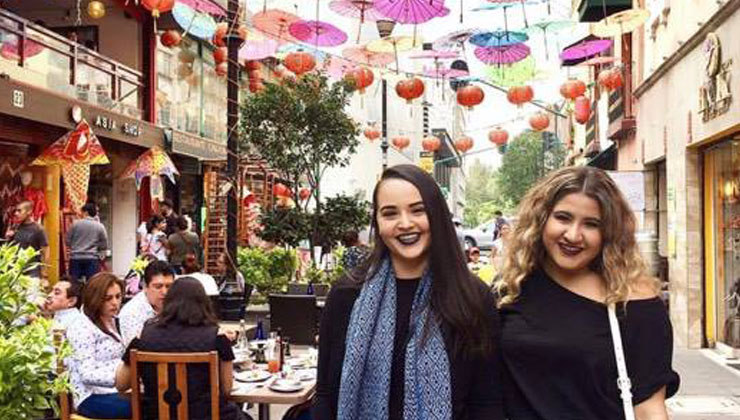 Two students stand under pink, yellow, blue, and peach colored umbrellas near a shopping center in Mexico City, Mexico.