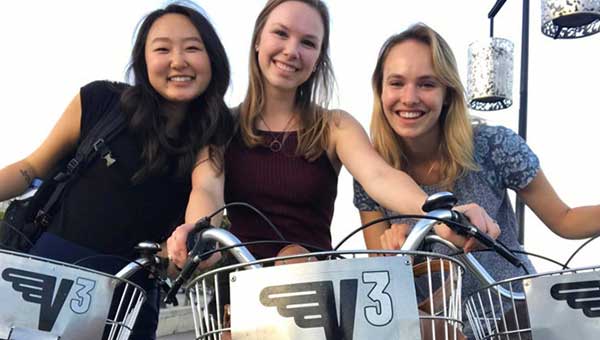 group of three students posing for camera while standing with bikes