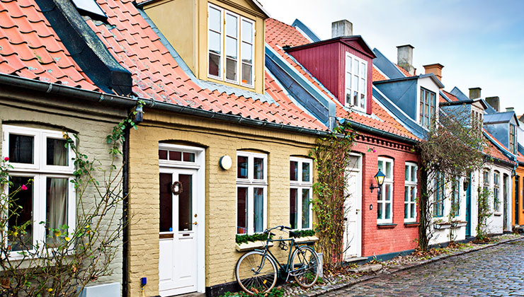 Yellow, peach, orange, red, and blue accents houses on a cobblestone street in Aarhus, Denmark.