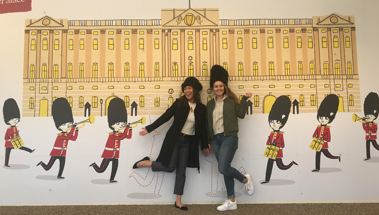 Two students posing near a wall with an illustration of Buckingham Palace in London, England.