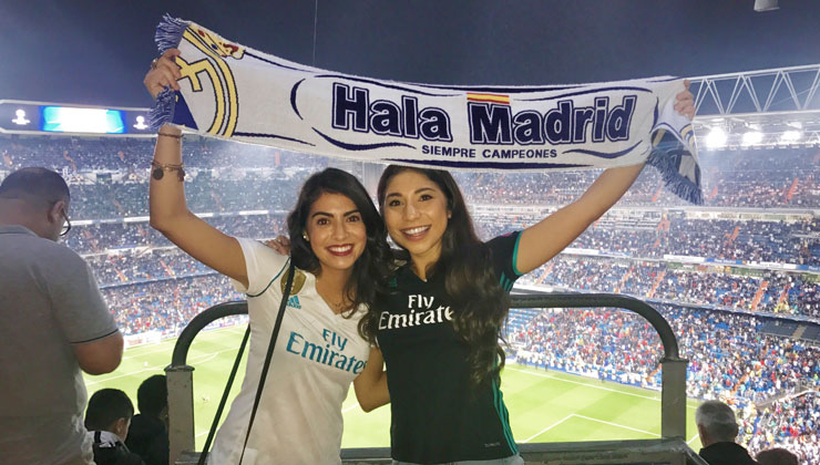 Two students at a Real Madrid game holding up a scarf that says Hala Madrid in Spain. 