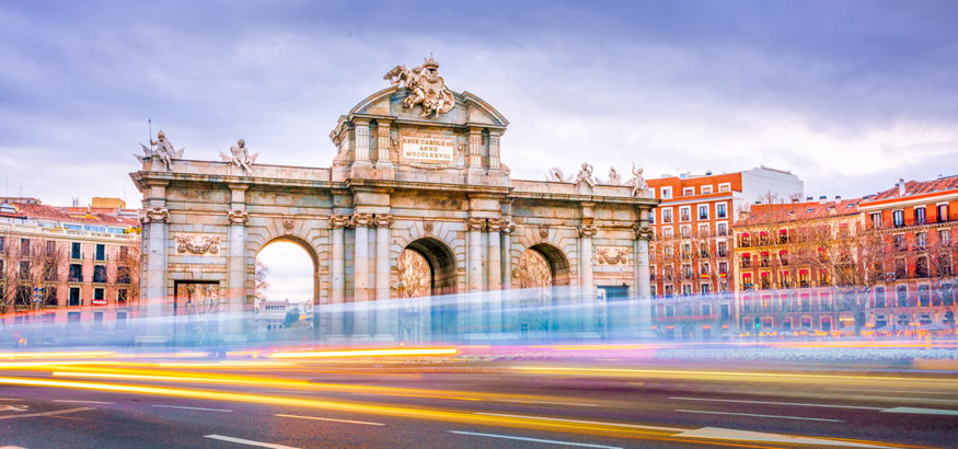 A shot of The Alcala Door (Puerta de Alcala), a post-Roman triumphal arch with cars passing by and buildings in the background in Madrid, Spain. 
