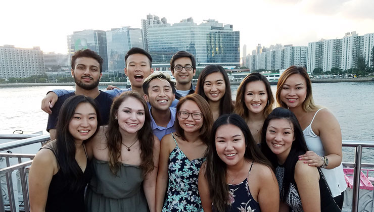 Twelve students smiling on on a cruise ship with a view of the Hong Kong skyline in the background.