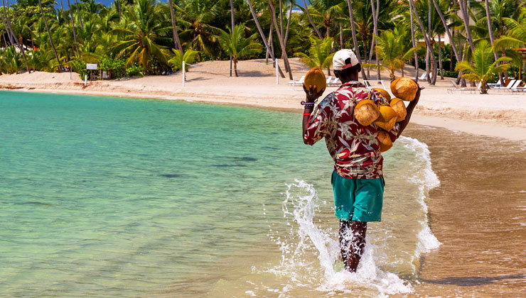 Coconut salesman walks in the turquoise water holding coconuts at a beach in the Dominican Republic.