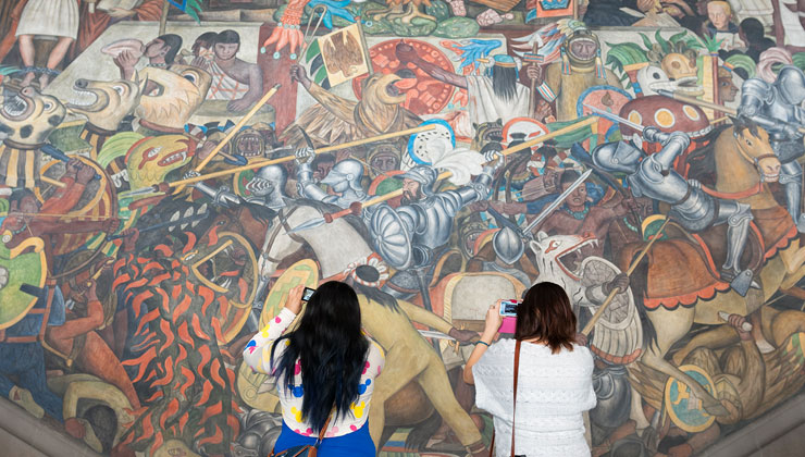 Two students take photos of the open-air mural near the steps of the National Palace in Mexico City, Mexico. 