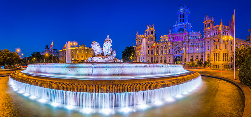 Spotlights illuminating the 18th Century fountain of Cybele overlooked by the iconic towers of the Palacio de Cibeles colourfully lit against the deep blue dusk skies above the Plaza de Cibele.