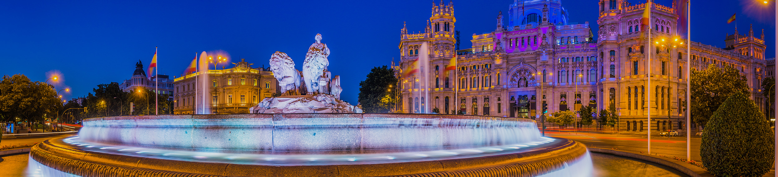 Spotlights illuminating the 18th Century fountain of Cybele overlooked by the iconic towers of the Palacio de Cibeles colourfully lit against the deep blue dusk skies above the Plaza de Cibele.