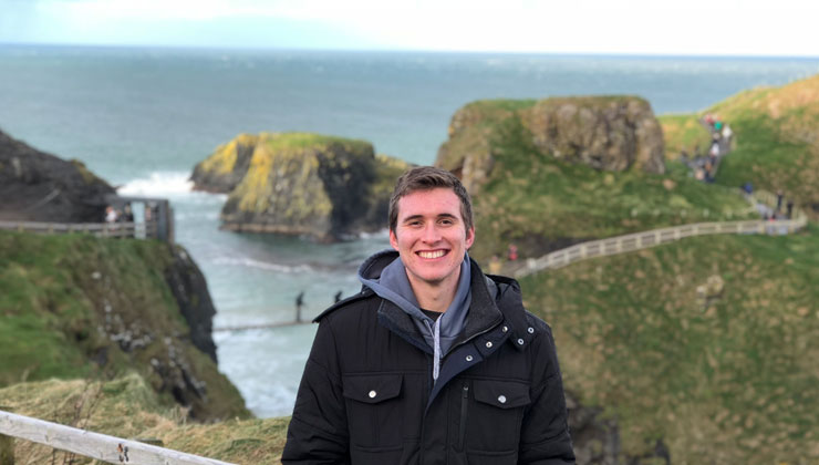 Jacob Huls smiling with a view of the Carrick-a-Rede Rope Bridge in County Antrim, Northern Ireland.