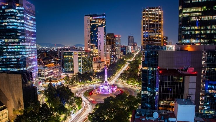 Skyscrapers lit up at nightime surrounding a fountain in a vibrant city center