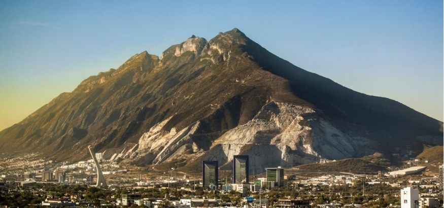 Sunlight rising over a large mountain, the skyline of Monterrey in the foreground.