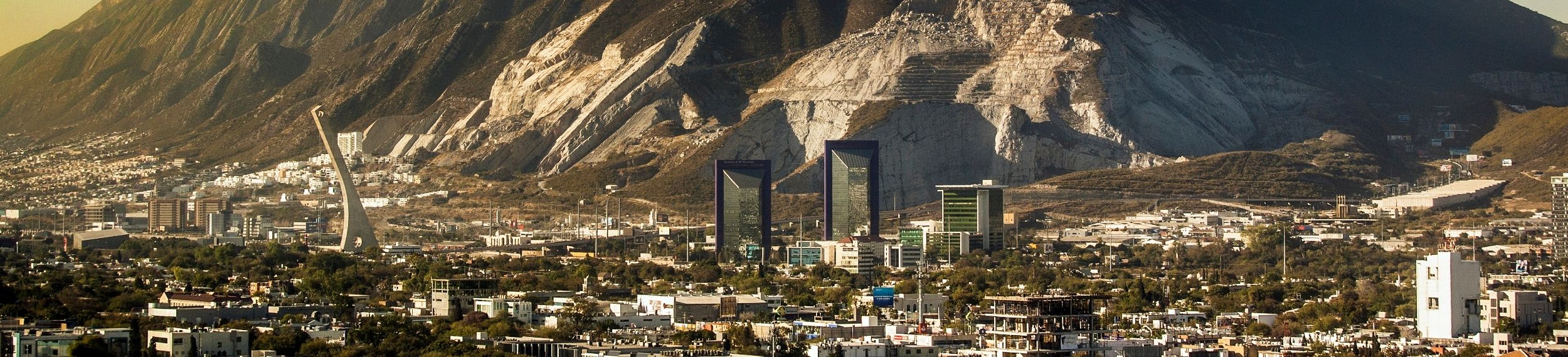 Sunlight rising over a large mountain, the skyline of Monterrey in the foreground.