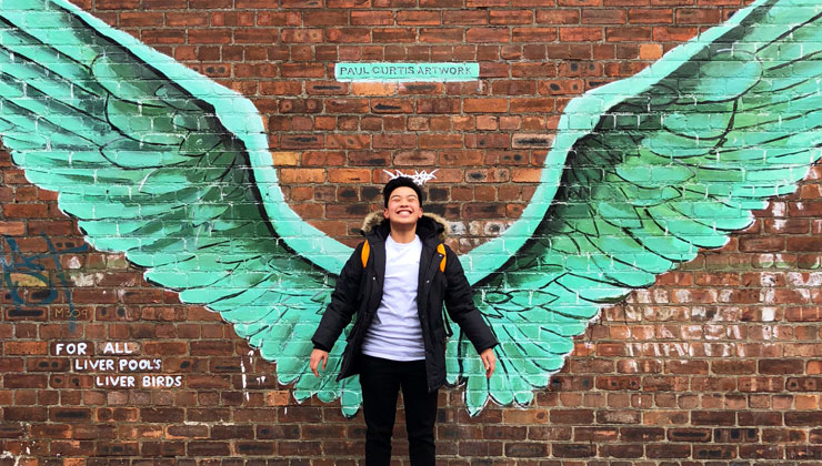 A student standing in front of mural of wings in Liverpool, England.