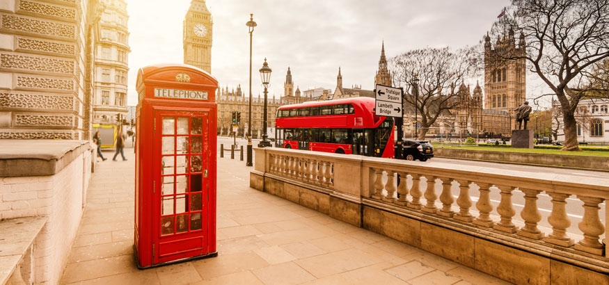 A red telephone booth with a double decker bus and Big Ben in the background in London England