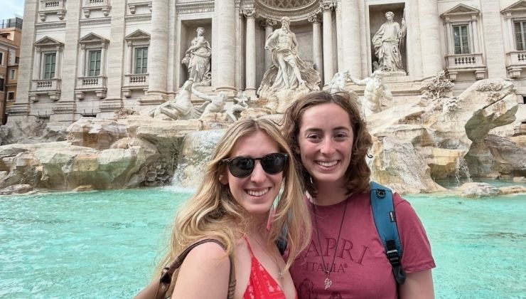 Two students smile and pose for a photo in front of the Trevi Fountain