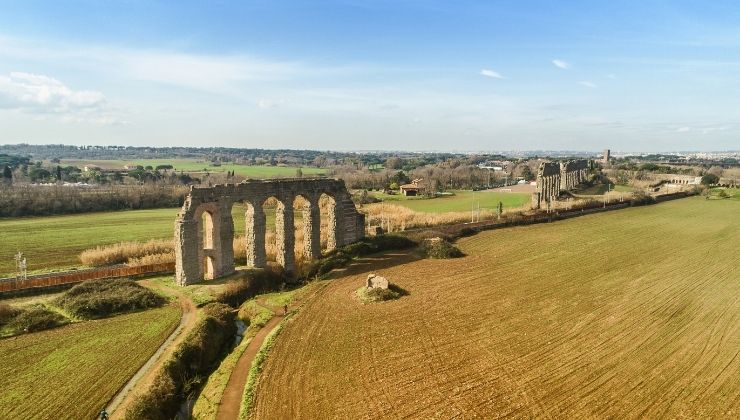 Aerial view of large stone structure with columns in a large grasy field, on a sunny day.
