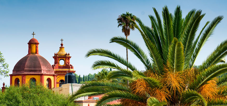 Church next to large palm trees with a view of Bernal in QuerétaroState, Mexico.