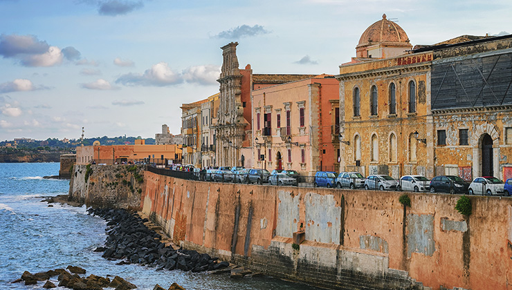 Colorful amber buildings line an embankment on the Mediterranean Sea in Syracuse, Sicily, in Italy. 