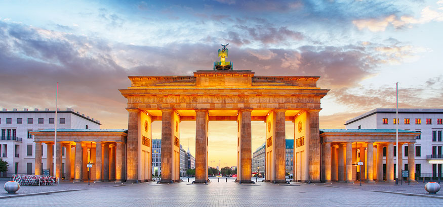 Brandenburg Gate lit up with an orange glow at dusk in Berlin, Germany.