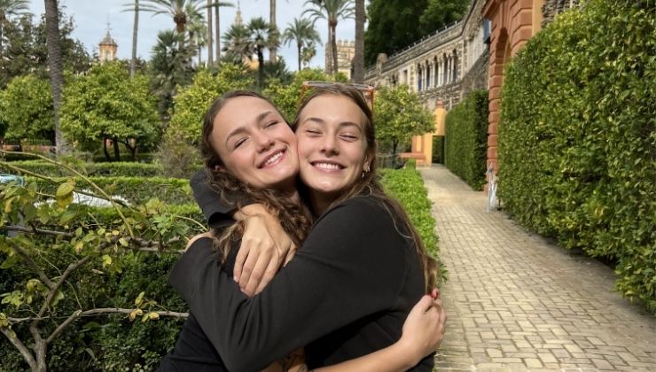 Two friends hug in a park, surrounded by lush greenery and palm trees.