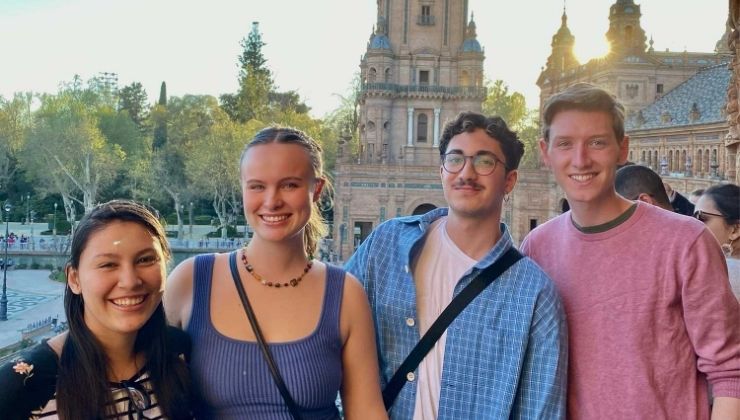 Four people smiling and posing for a photo in front of traditional Spanish architecture, at sunset.