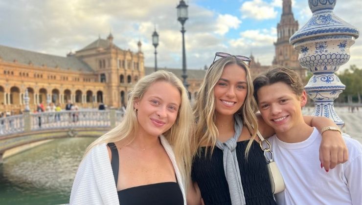 Three people pose in front of a river and castle-like architecture in Seville, Spain