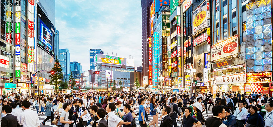 Pedestrians crossing the busy intersection with colorful urban buildings and signs in Shinjuku, Tokyo, Japan