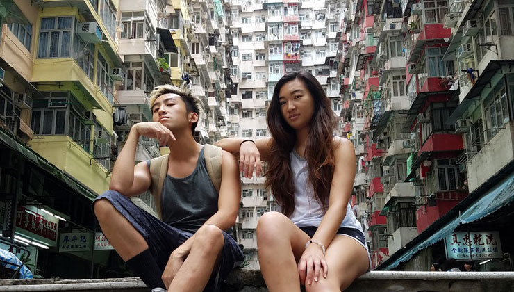 Two students sit on some steps with colorful buildings in the background at King’s Road Quarry Bay in Hong Kong. 