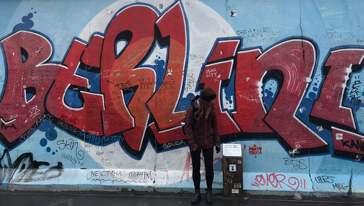 Student in front of large, red graffiti on the Berlin Wall in Germany.