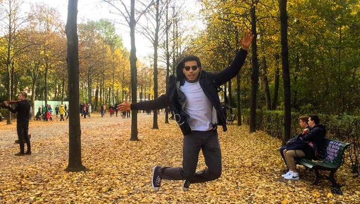 Student jumps in the air on a street covered in yellow leaves in Berlin, Germany.