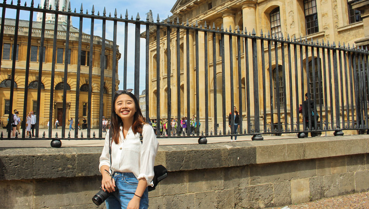 A students smiles in front of The Radcliffe Camera at All Souls College