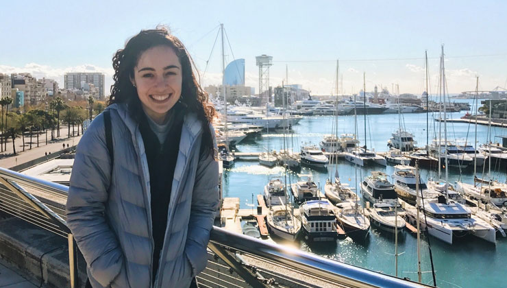 Student smiling at the camera with a view of the pier in Barcelona, Spain.