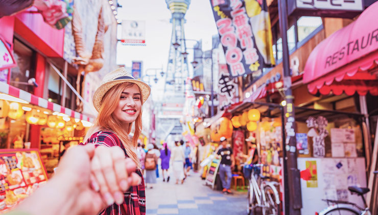 Two tourists explore the bright and colorful Shinsekai neighborhood in Osaka, Japan.