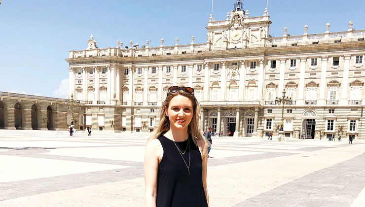 Female student standing in front of the Royal Palace of Madrid in Madrid, Spain.