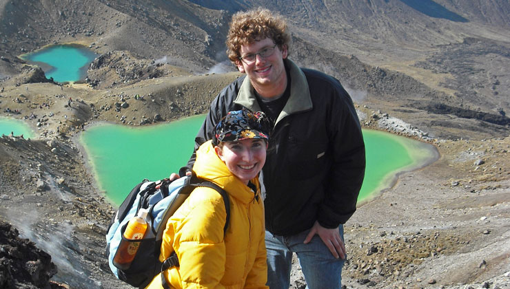 Two students standing on a hill with an active geothermal area in the background.
