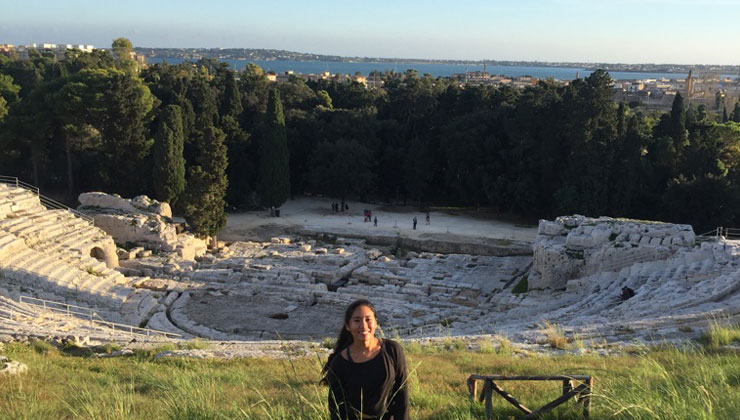 UC Irvine student poses in the grass above the empty Greek Theatre of Syracuse in Italy.