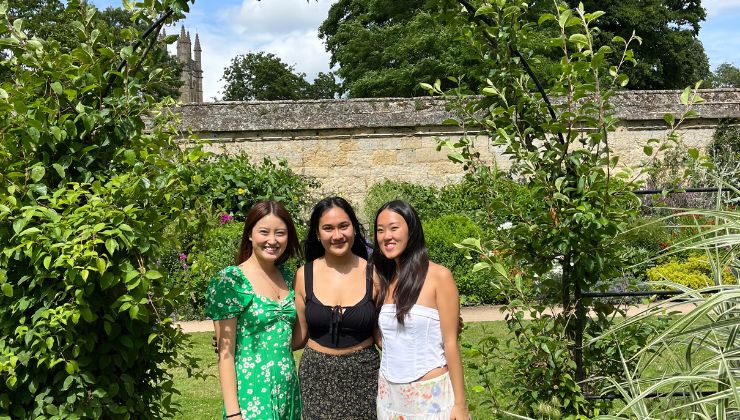 Three people stand side by side in a lush garden and smile for a photo