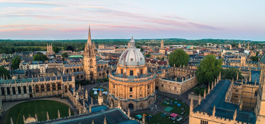 Aerial view of the Radcliffe Camera building surrounded by historic university architecture in Oxford, England, at sunset.