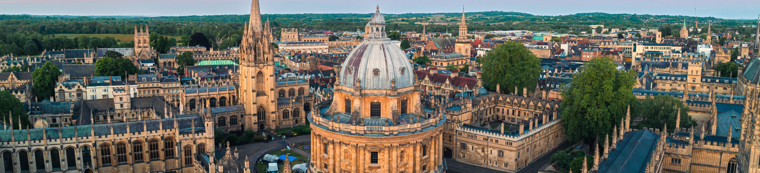 Aerial view of the Radcliffe Camera building surrounded by historic university architecture in Oxford, England, at sunset.