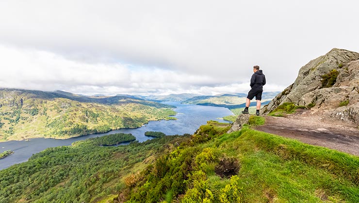 A hiker looks out from the mountain Ben A'an to Loch Katrine in the Trossachs, Scotland.