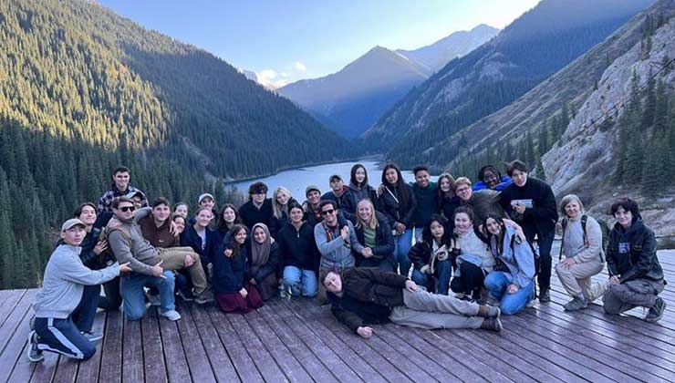 Group pose in front of Big Almaty Lake surrounded by mountains.
