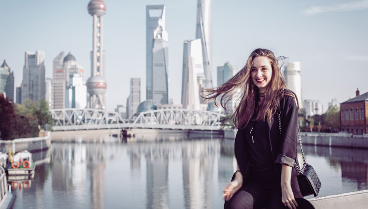 Female student in the foreground with the river and downtown skyline in the background in Shanghai, China.