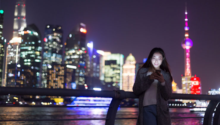 Student on her phone at night with the Oriental Pearl TV tower and downtown buildings in the background. 