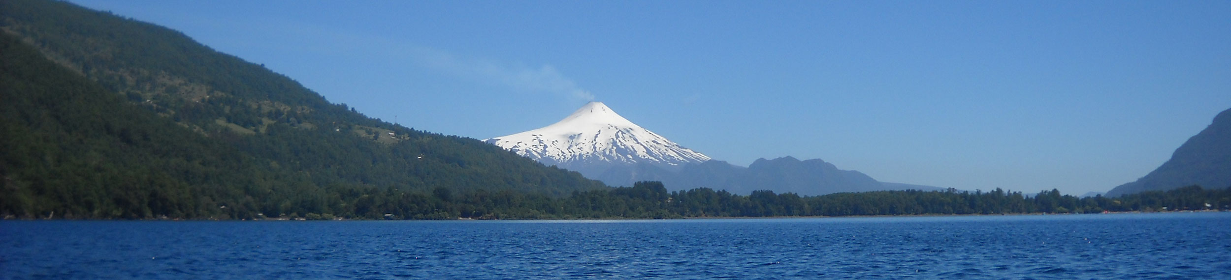 The snow covered Volcán Villarrica behind a big blue lake in Villarrica, Chile.