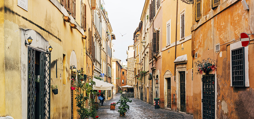 Golden walls, color-filled flower pots, and cobblestones line a street in the Trastevere neighborhood