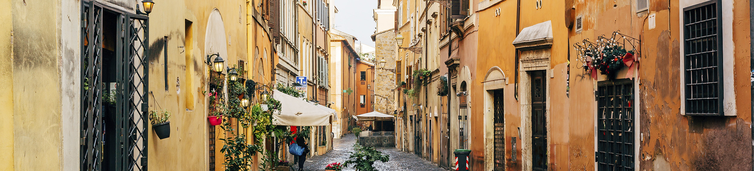 Golden walls, color-filled flower pots, and cobblestones line a street in the Trastevere neighborhood in Rome.