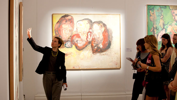 A group of students on our tour looking at a painting. The tour guide is also looking and point at the artwork.