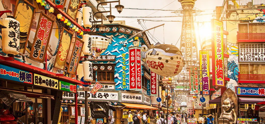 The colorful Shinsekai District glows in the bright sunshine with Tsutenkaku Tower in the background in Shinsekai, Osaka, Japan