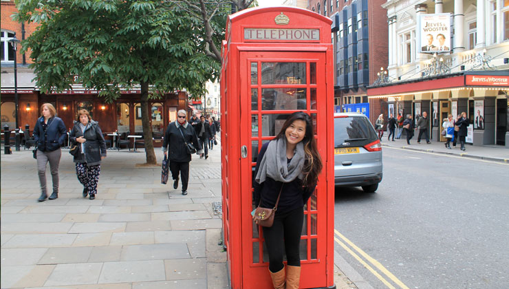 A student standing next to a red phone booth in London, England. 